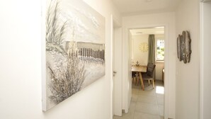 A hallway with a large abstract painting, a dining area with a wooden table and chairs, and a clock on the wall. - Beachfront vacation rental with a terrace, access to the pool and sauna - Rex Rugia H-1010 - (Göhren)