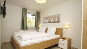 A neatly made bed with white linens, a wooden headboard, a bedside table with a lamp, and a painting on the wall. - Beachfront vacation rental with a terrace, access to the pool and sauna - Rex Rugia H-1010 - (Göhren)
