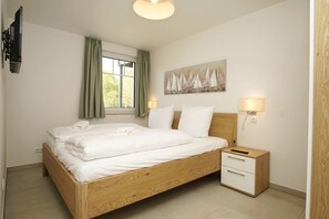 A neatly made bed with white linens, a wooden headboard, a bedside table with a lamp, and a painting on the wall. - Beachfront apartment with terrace, use of swimming pool and sauna - Rex Rugia apartment 15-3 (Göhren)