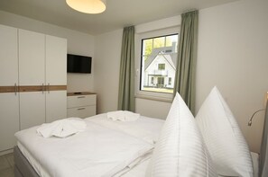 Une chambre à coucher avec un lit, une télévision, une fenêtre avec des rideaux et une vue sur une maison.