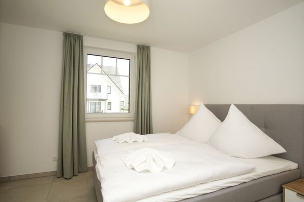 A neatly made bed with white linens, a grey headboard, and two bedside lamps.