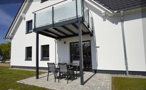A modern house with a covered patio area featuring a table and chairs.