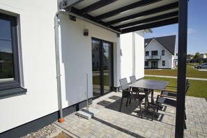 Un bâtiment moderne doté d’un patio couvert, d’une table avec des chaises et offrant une vue dégagée sur le quartier environnant.