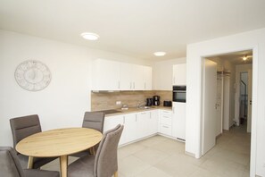 A modern kitchen with white cabinets, a wooden countertop, and a round dining table with chairs. - Beachfront vacation rental with a terrace, pool access, and a sauna - Rex Rugia - Rex (Göhren)