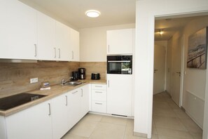 A modern kitchen with white cabinets, a wooden countertop, a built-in oven, and a coffee maker.