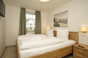 A hotel room with a bed, a nightstand, a lamp, a painting, and a window with curtains. - Beachfront vacation rental with a terrace, access to the pool and sauna - Rex Rugia H-1010 - (Göhren)
