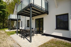 A modern house with a glass conservatory, outdoor seating, and a paved patio.
