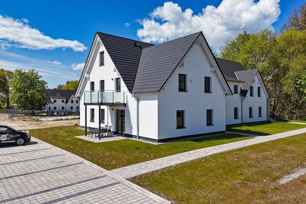 A modern two-story house with a balcony, a paved driveway, and a well-maintained lawn.