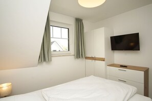 A bedroom with a bed, a TV mounted on the wall, a wardrobe, and a window with curtains. - Beachfront vacation rental with a balcony; access to the pool and sauna - Rex Rugia - Rex Rugia (Göhren)
