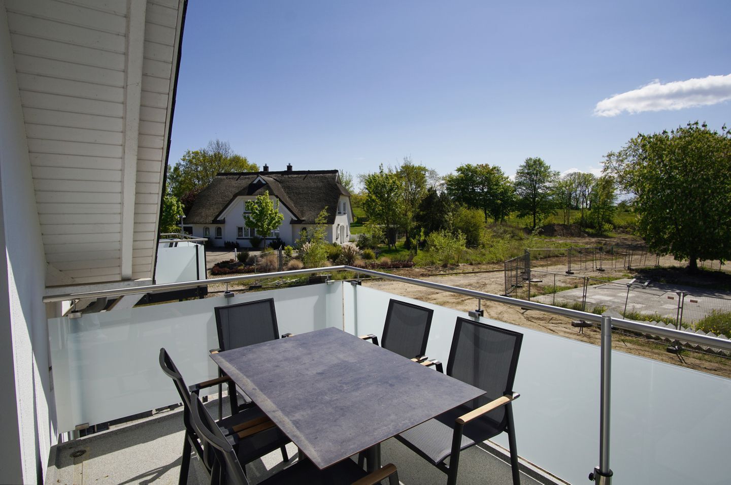 A balcony with a table and chairs, overlooking a garden and a house.