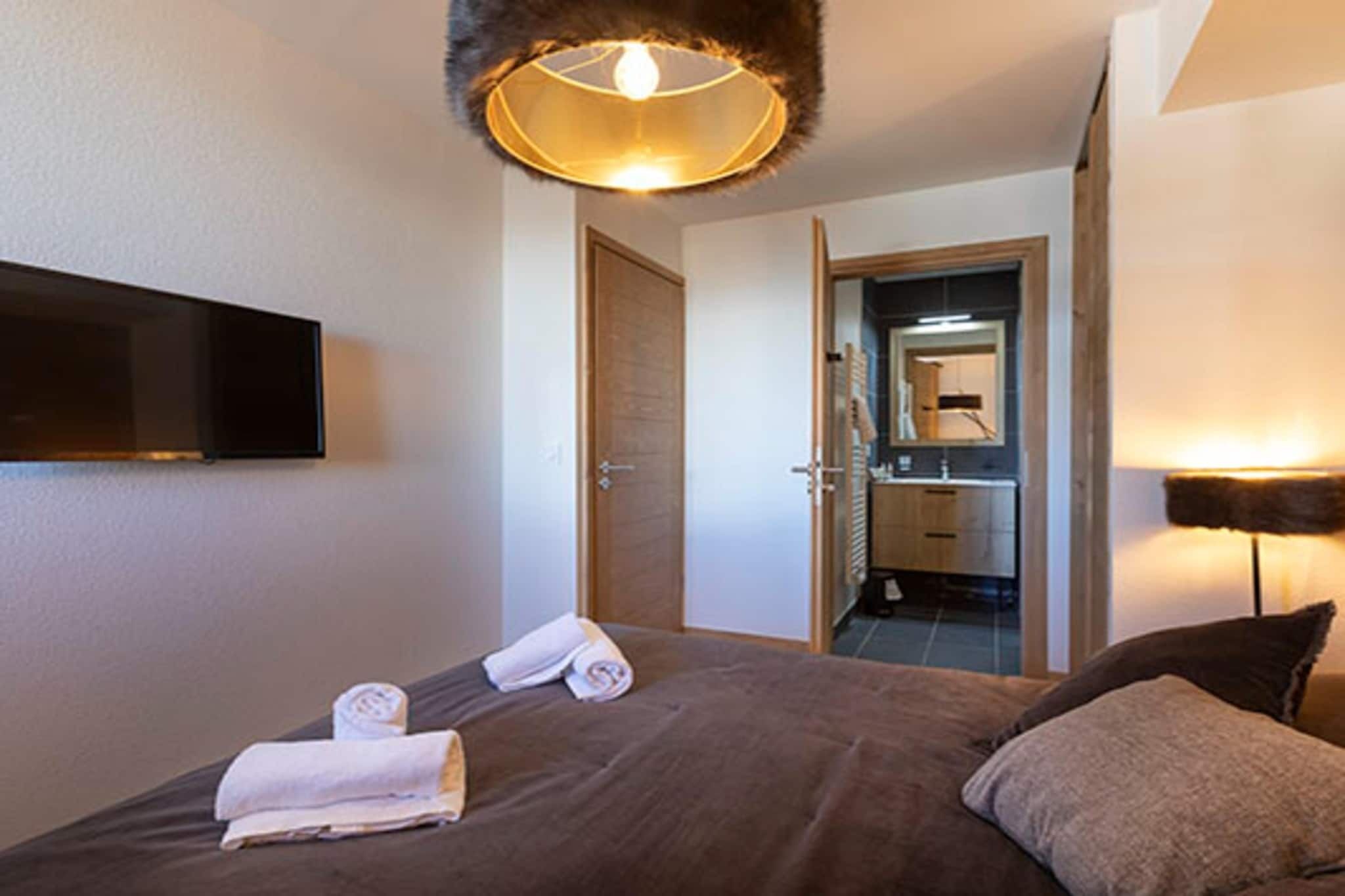 Une chambre d’hôtel comprenant un lit, un téléviseur à écran plat fixé au mur, une salle de bain avec un miroir et une porte donnant sur une autre pièce.