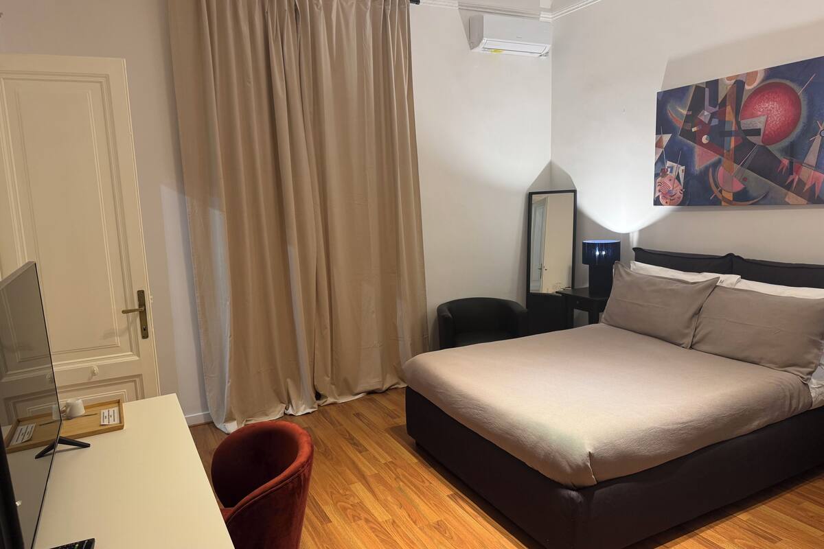 Hotellihuone, jossa on sänky, työpöytä, tuoli, pöytävalaisin, peili ja taulu seinällä.