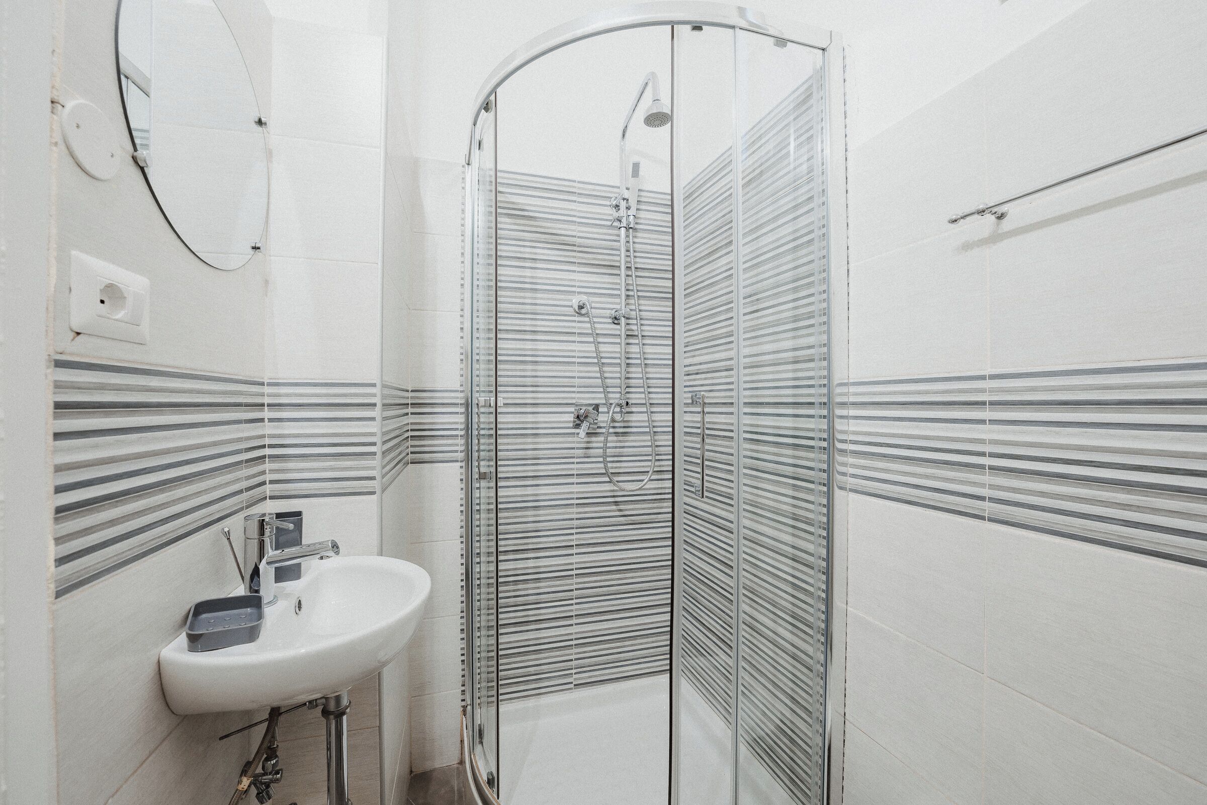 A modern bathroom with a glass-enclosed shower, a white sink, and striped wall tiles.