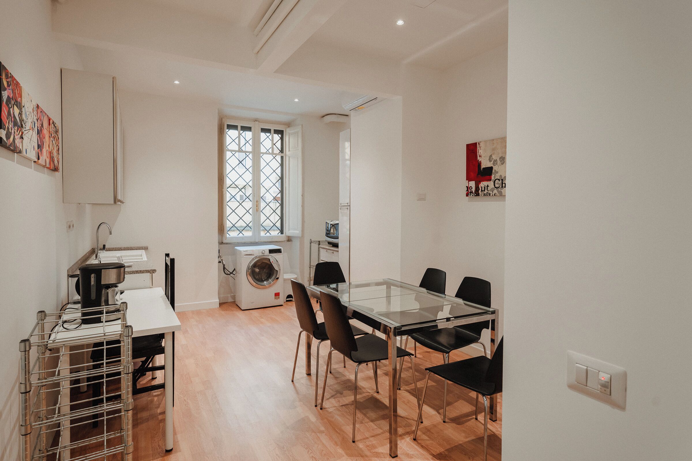 A modern kitchen with a dining area, including a table, chairs, and a washing machine.