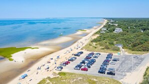 An aerial view of a beachside parking lot adjacent to a sandy beach with a clear view of the ocean.