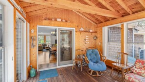 A wooden interior with a wooden ceiling, a sliding glass door leading to a living area, and a blue cushioned chair.