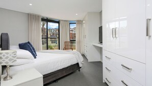Una habitación de hotel moderna con una cama grande, un escritorio, un armario y un balcón con vistas a la ciudad.