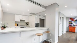 Una cocina moderna con armarios blancos, un refrigerador de acero inoxidable y dos taburetes de bar.
