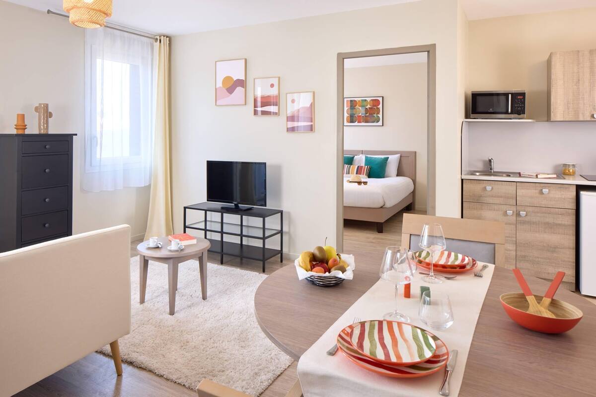 Moderni hotellihuone, jossa on ruokailutila, pieni keittiö ja sängystä avautuva kaunis näkymä.