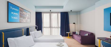 A hotel room with two beds, a purple sofa, a small table, and a large window with curtains.