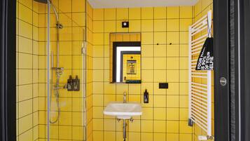 A bathroom with yellow tiles, a white sink, a mirror, and a shower.