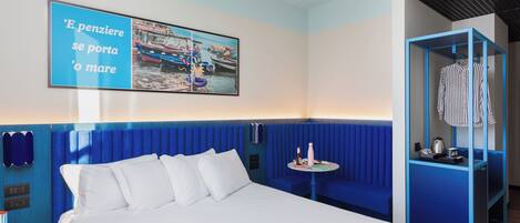 A hotel room with a bed, a blue accent wall, a small table with a bottle and a cup, and a clothing rack.