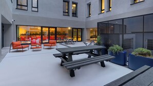 Un espace extérieur aménagé en terrasse, avec une table de pique-nique en bois, des chaises orange et des jardinières bleues.