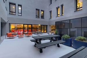 An outdoor patio area with a wooden picnic table, orange chairs, and blue planters.