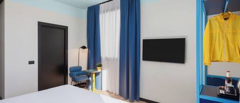 Una habitación de hotel moderna con una cama, un escritorio, una silla, un televisor y un armario con una chaqueta amarilla colgada.