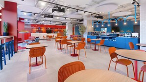 Un café moderne doté de plusieurs espaces de détente, notamment des tables et des chaises, ainsi que d’un comptoir avec un fond bleu.