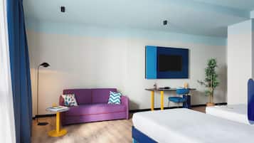 Una habitación de hotel moderna con un sofá púrpura, una mesita redonda pequeña, un escritorio con una silla, una cama y una planta en maceta.