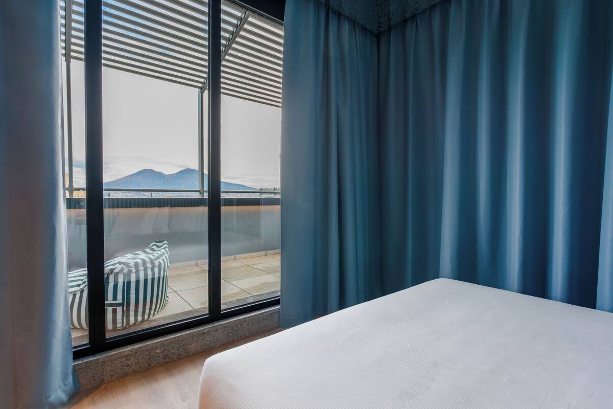 Ett hotellrum med ett stort fönster, en säng och utsikt över ett avlägset berg.