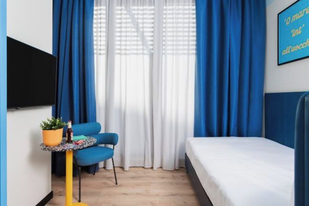 Une chambre à coucher avec un lit, une petite table sur laquelle est posée une plante, une chaise et un téléviseur fixé au mur.