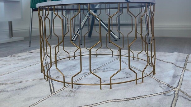 Een moderne eetruimte met een glazen tafel en stoelen, een geometrisch metalen tafelvoet en een kamerbreed tapijt.