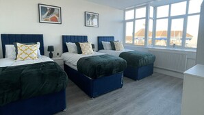 Een moderne hotelkamer met drie bedden, grote ramen en kunstwerken aan de muur.