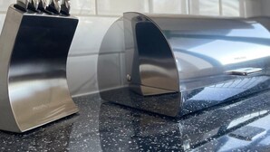 Een keukenblad met een messenblok en een roestvrijstalen apparaat, waarschijnlijk een koffiezetapparaat of espressomachine.