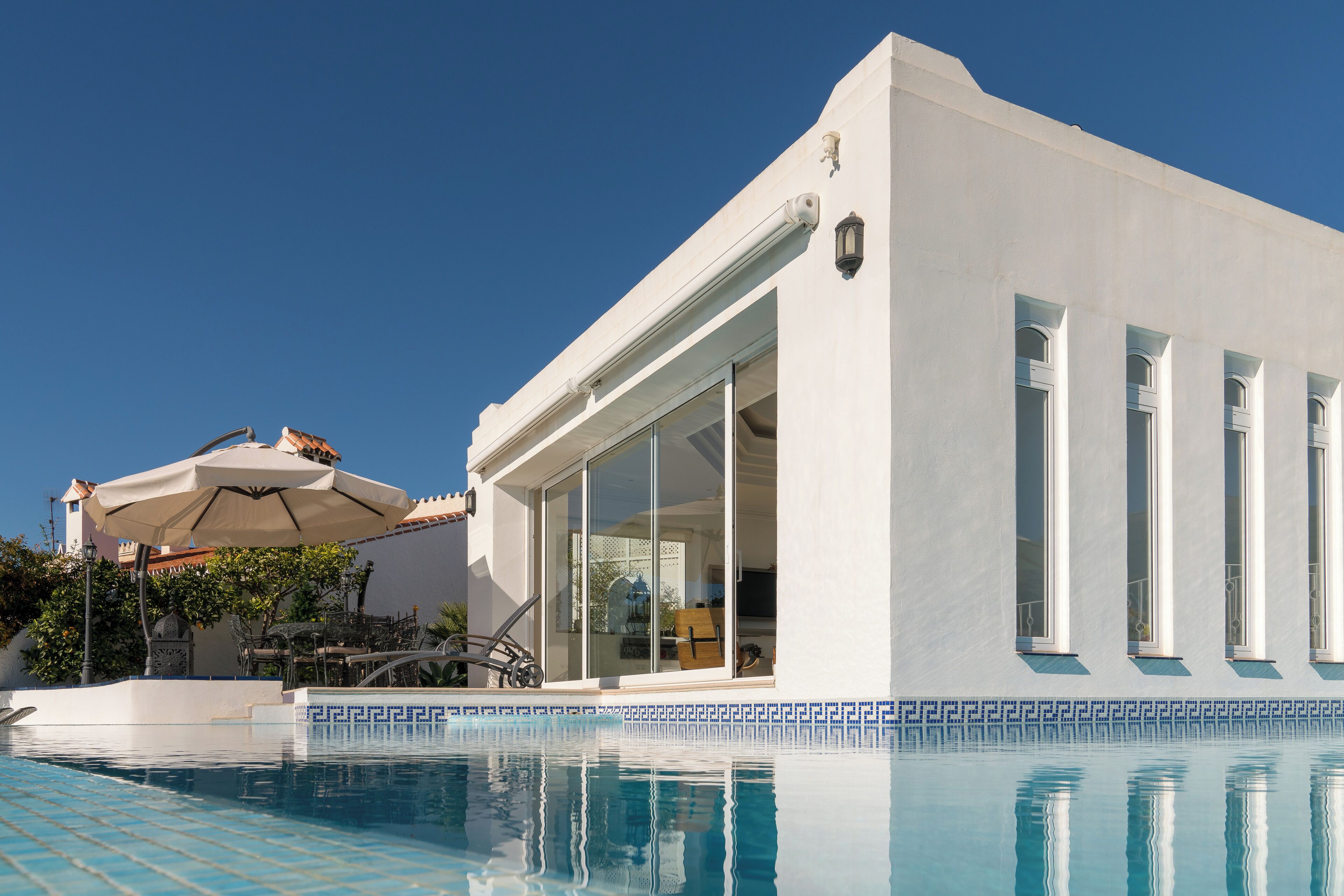 A modern white building with a pool, large windows, and a covered patio area.