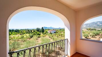 A balcony with a view of a rural landscape, including trees and distant mountains.