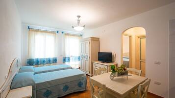 A room with two beds, a TV, a table with chairs, and a small kitchen area.