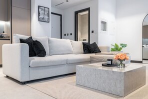 Un salon moderne avec un canapé gris clair, des coussins noirs, une table basse en marbre et un tableau encadré représentant la Tour Eiffel.