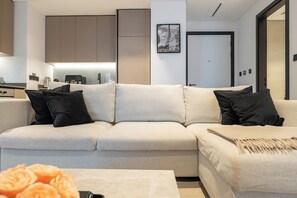 A modern living room with a sectional sofa, a coffee table, and a kitchen area in the background. - Luxury 1-Bedroom Apartment, Burj Khalifa Views & Infinity Pool, Dubai Mall (Dubai)
