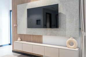 Un salon moderne avec un téléviseur à écran plat fixé sur un mur texturé, une console minimaliste en dessous et un grand vase décoratif.