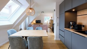 Et moderne køkken med en træbordplade, lysegrå skabe og et spiseområde med et træbord og grå stole.