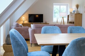 Un soggiorno moderno con un tavolo in legno, sedie blu, un divano rosa e un televisore su un mobile.