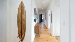 En gang med trægulv, et surfbræt monteret på væggen, et spejl og et lille bord med en lampe.