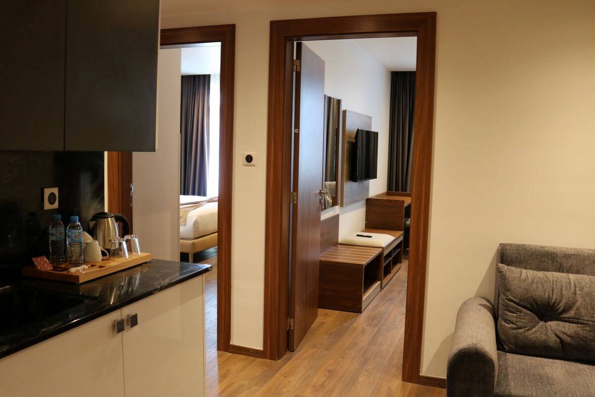 A modern hotel room with a kitchenette, a sofa, and a TV.
