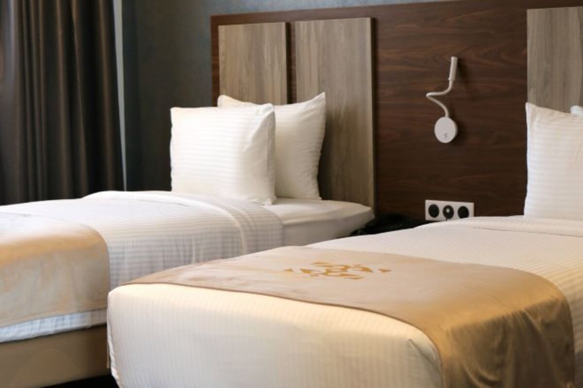 Une chambre d’hôtel avec deux lits, une tête de lit en bois et une table de chevet avec une lampe.