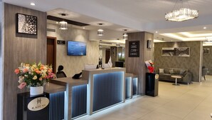 A hotel reception area with a modern design, including a reception desk, a television screen, and a chandelier. - Hôtel EL AZIZ INN (Algiers)