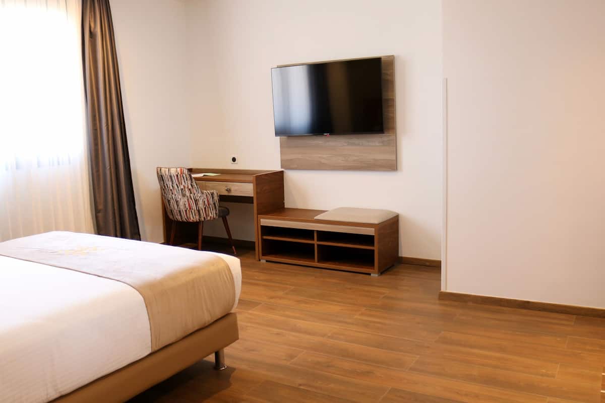 A hotel room with a bed, a desk, a chair, and a flat-screen TV mounted on the wall.