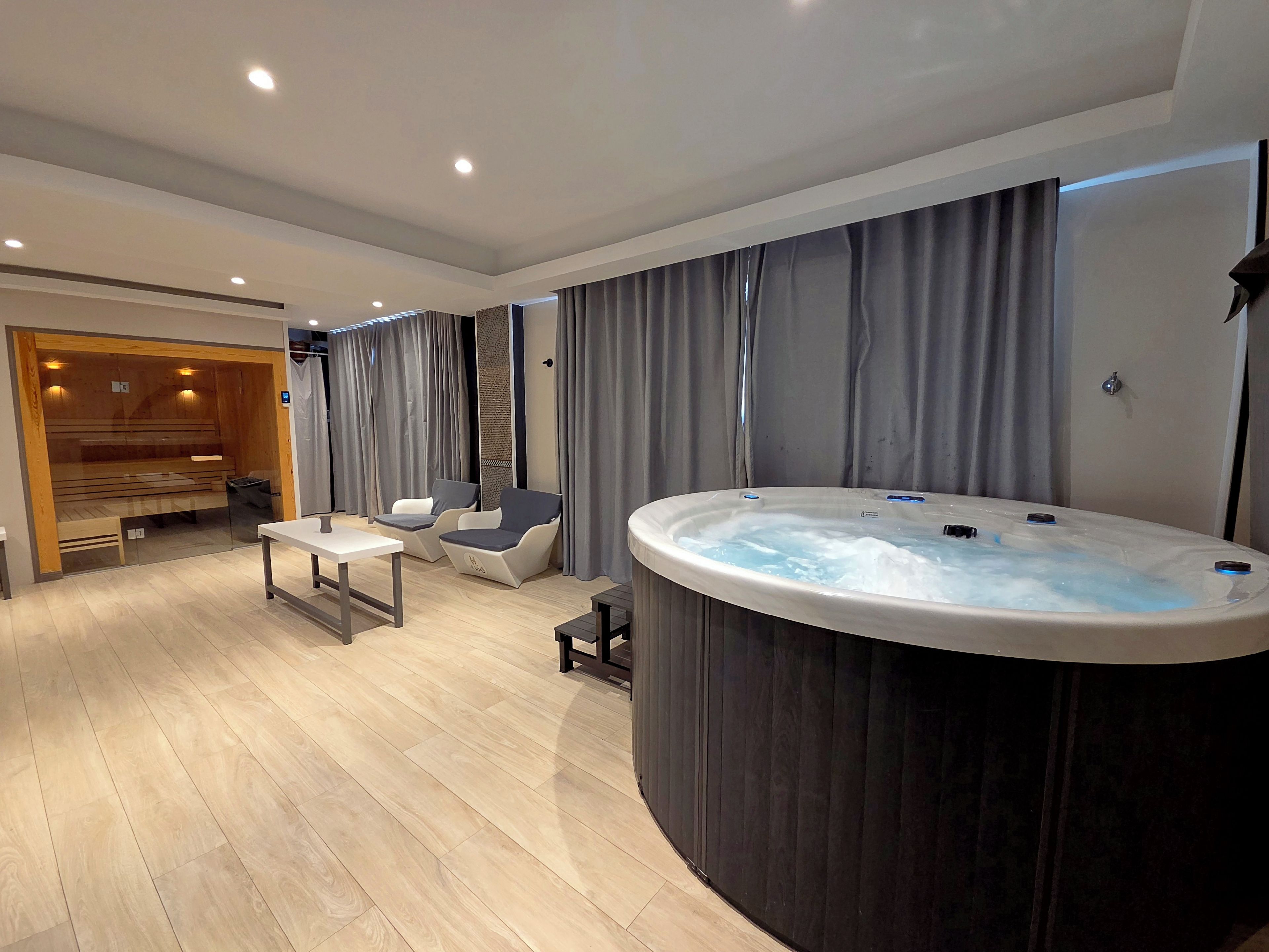Un moderno cuarto de spa con bañera de hidromasaje, zona de estar y sauna de madera.